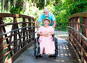 An older man pushing an older woman in a wheelchair.